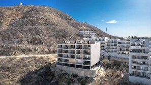 Un immeuble résidentiel moderne à plusieurs étages, doté de balcons, situé dans une zone vallonnée où la végétation est clairsemée.