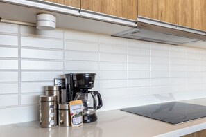 Une cuisine avec des carreaux blancs, une machine à café, une bouilloire, un thermos et une boîte de capsules de café.