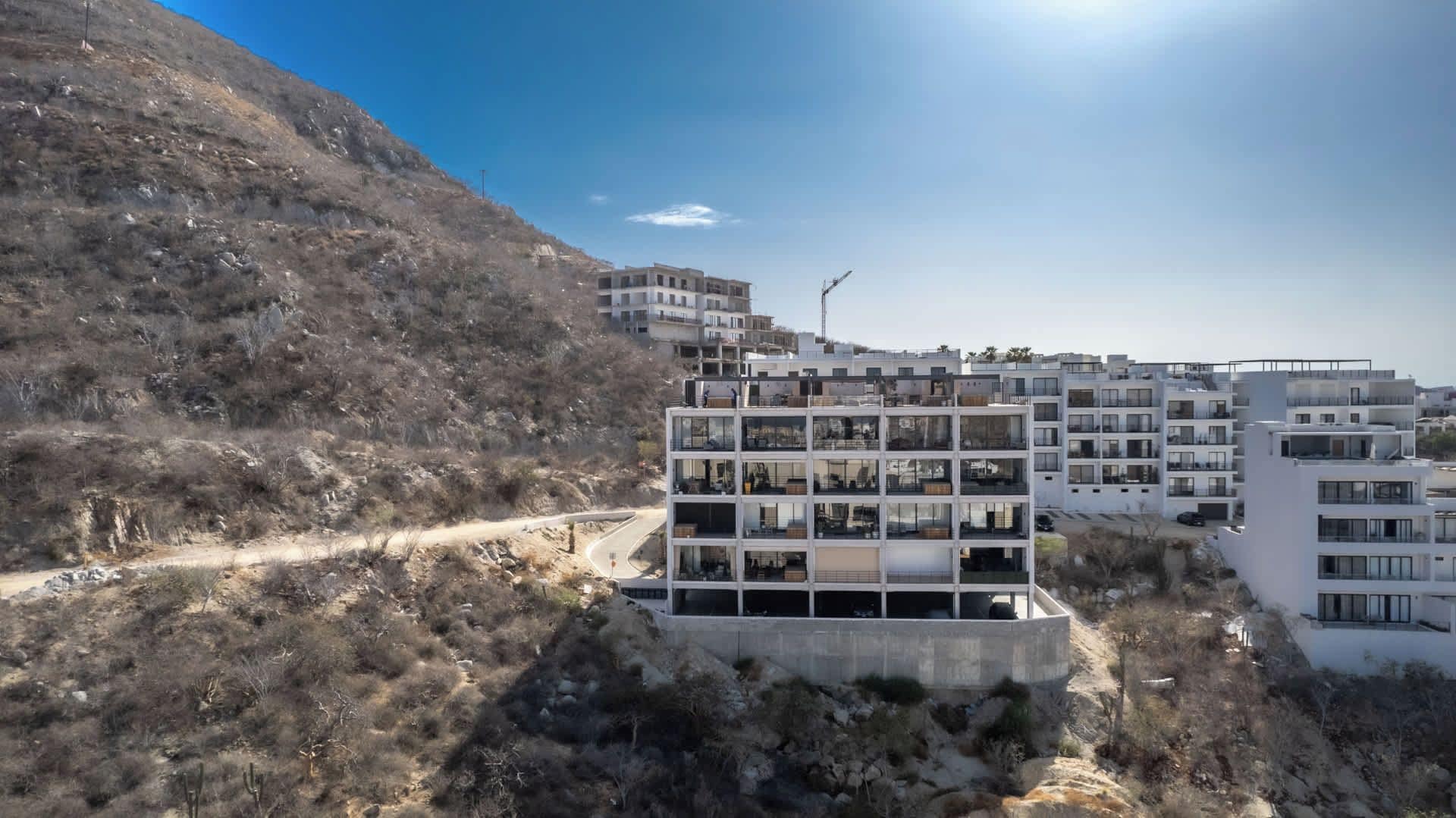 A multi-story residential building with balconies, situated on a hillside with a clear sky.