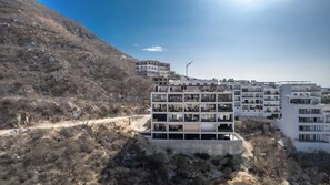 Un immeuble résidentiel à plusieurs étages, doté de balcons, situé sur une colline et offrant une vue sur un ciel dégagé.