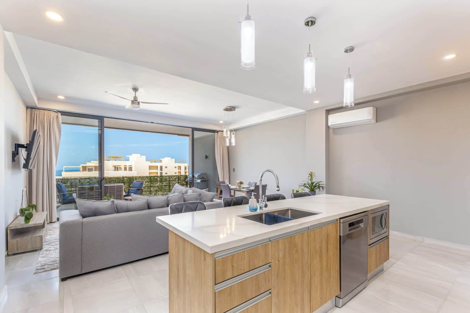 A modern kitchen with a central island, a dining area with a sofa, and a view of buildings through large windows.