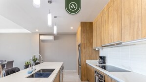 Une cuisine moderne avec des meubles en bois, un plan de travail blanc, un four encastré et des luminaires suspendus.