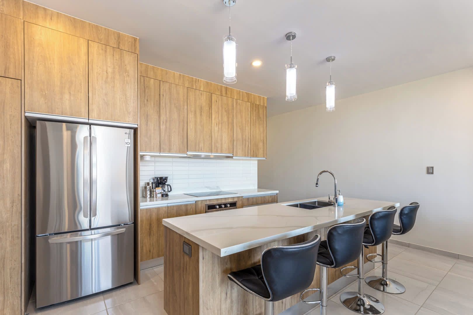 Una cocina moderna con un refrigerador de acero inoxidable, armarios de madera, una isla central con taburetes de bar e iluminación colgante.