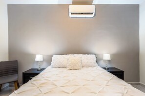 A bedroom with a bed, two bedside tables, two lamps, and an air conditioning unit.