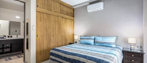 A bedroom with a bed, bedside tables, a wardrobe, and a bathroom with a mirror and sink.