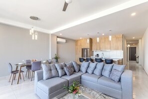A modern living room with a sectional sofa, dining area, and kitchen. - New 2 BR Condo With Private Terrace - BBQ (Cabo San Lucas)