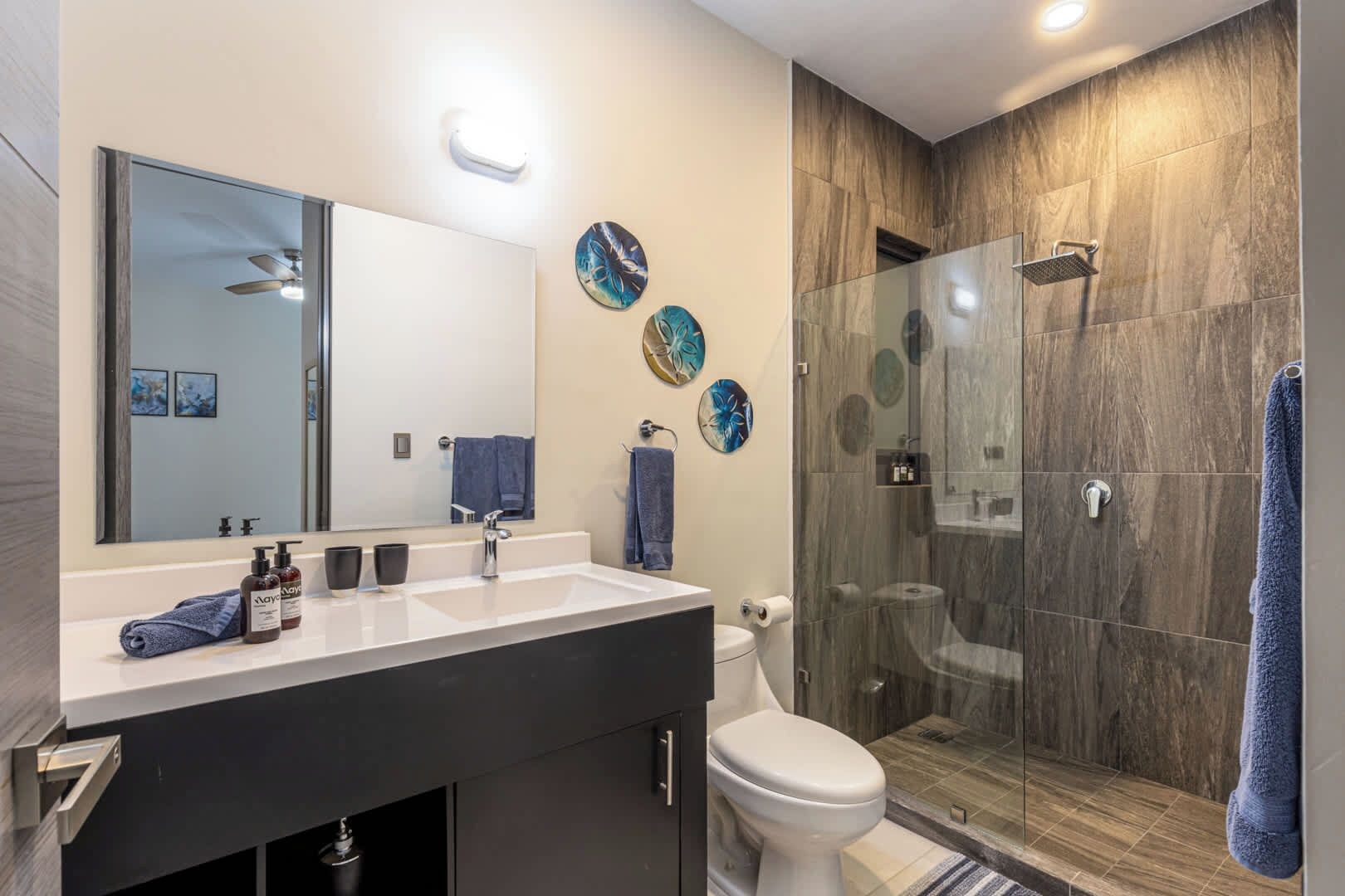 Un baño moderno con tocador de doble lavamanos, ducha con cerramiento de vidrio y protectores de pared decorativos.