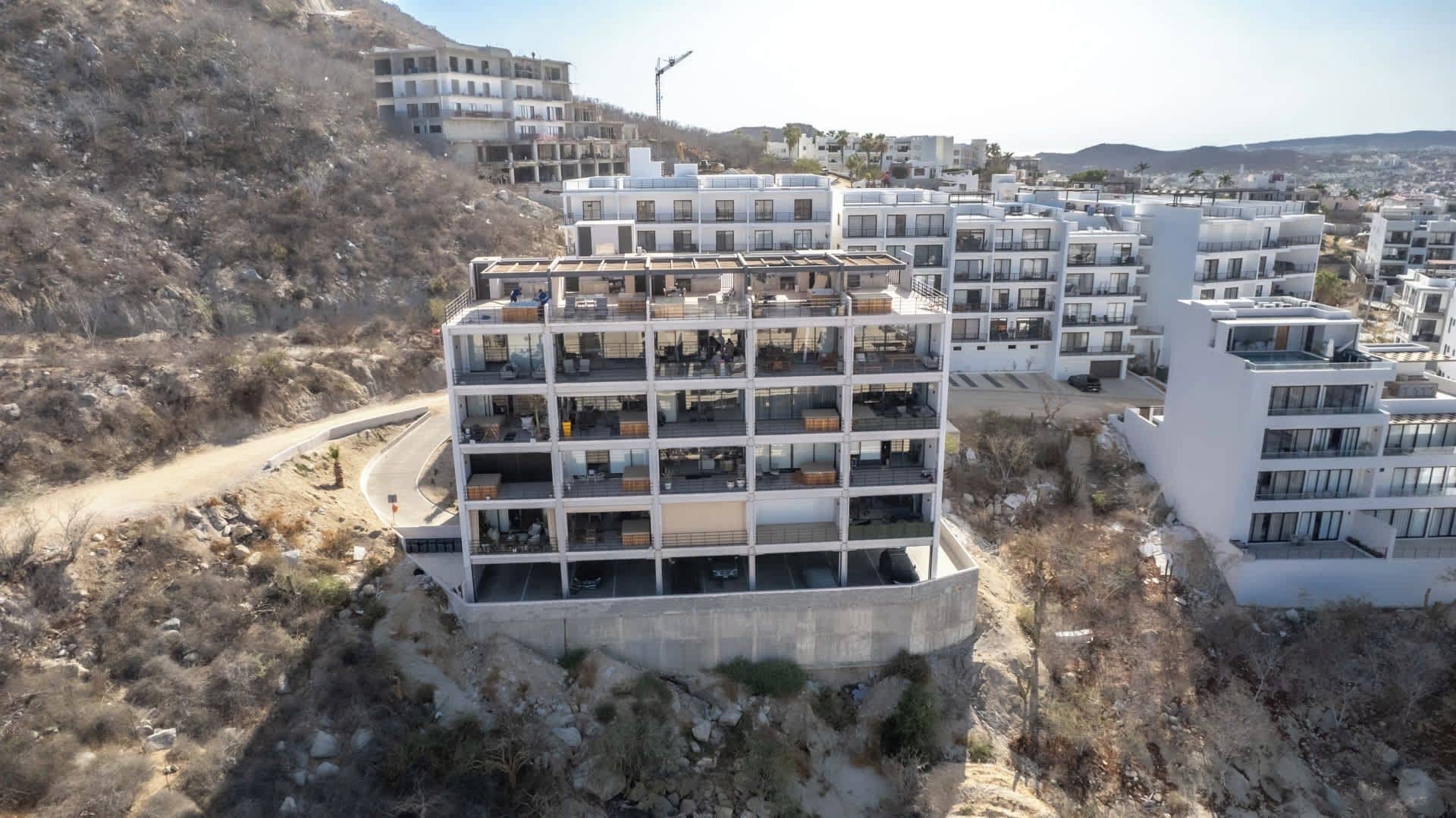 Un edificio residenziale a più piani con balconi, immerso in una zona collinare con altri edifici sullo sfondo.