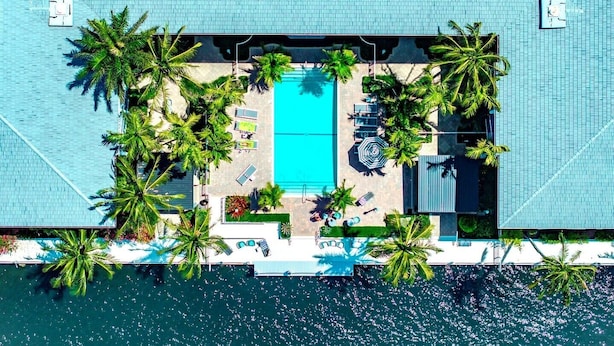 An aerial view of a resort with a central swimming pool surrounded by palm trees and lounge chairs. - Boca Waterfront Oasis: Walk to Beach + Pool, Hot Tub, Gym (Boca Raton)