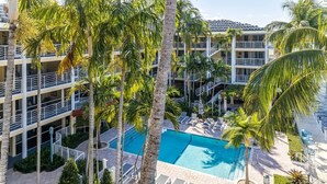 A multi-story hotel with a central swimming pool surrounded by palm trees and lounge chairs. - Boca Waterfront Oasis: Walk to Beach + Pool, Hot Tub, Gym (Boca Raton)