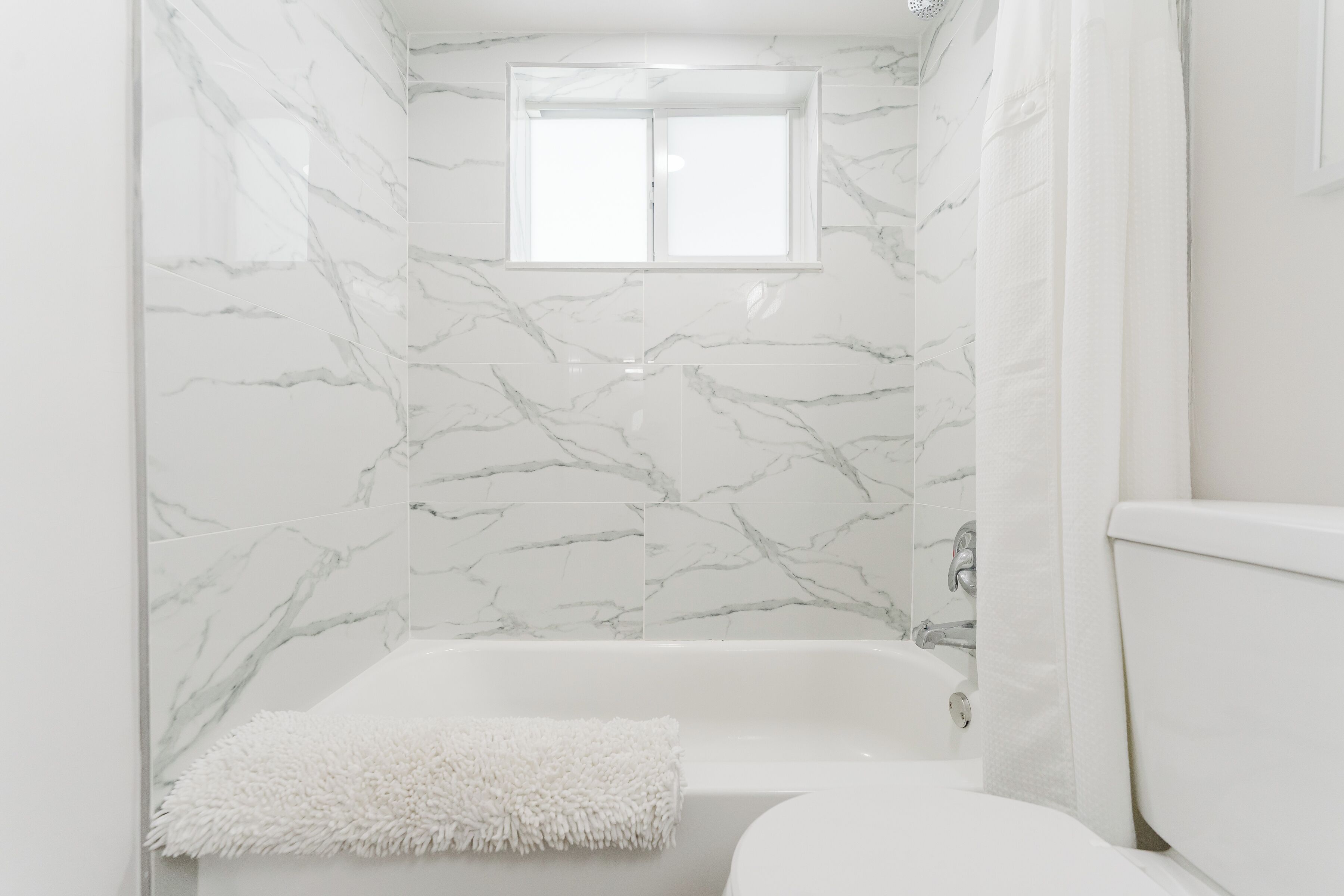 Ein Badezimmer mit einer weißen Badewanne, einem flauschigen weißen Handtuch und Wänden mit Marmoroptik.