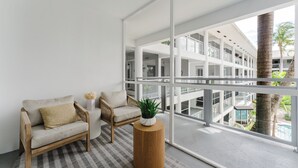 A modern room with a large window, two sofas, a round wooden side table, and a potted plant. - Boca Waterfront Oasis: Walk to Beach + Pool, Hot Tub, Gym (Boca Raton)