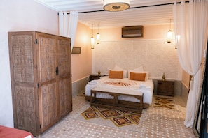 A bedroom with a large wooden wardrobe, a bed with a patterned bedspread, two bedside tables, and hanging lamps.