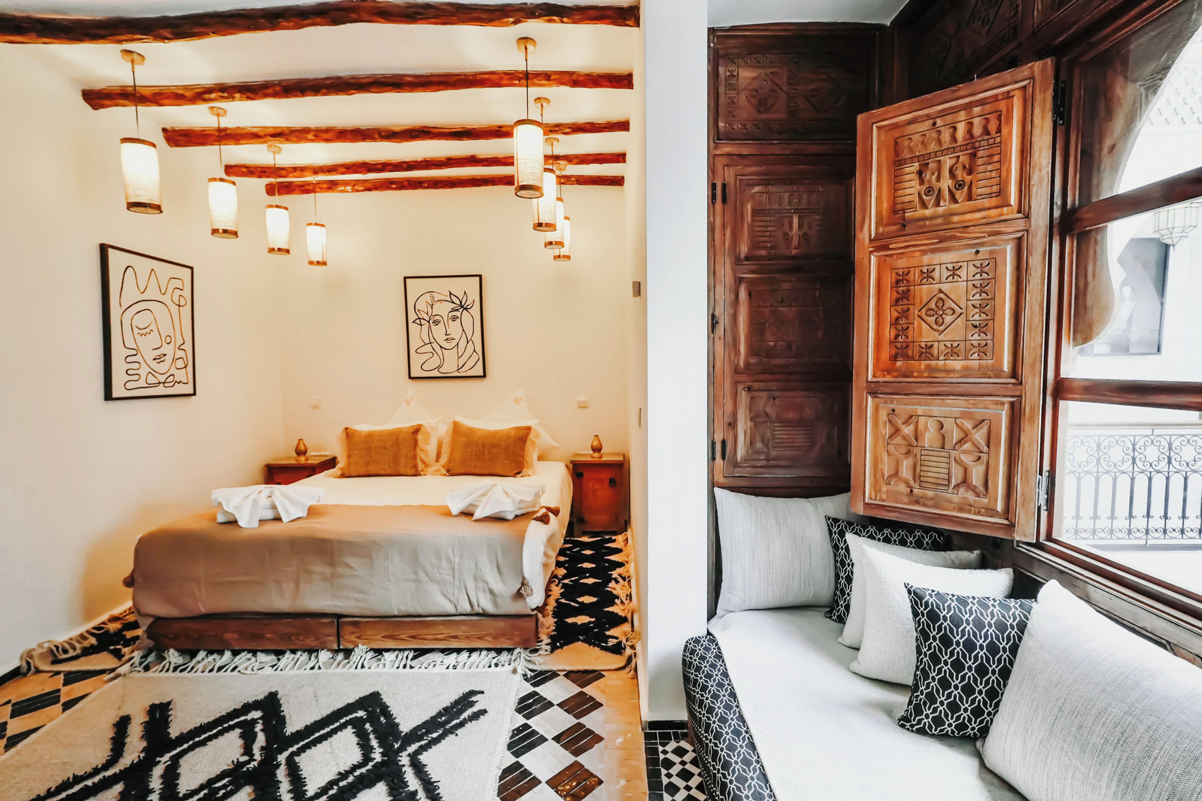 A bedroom with a bed, bedside tables, a patterned rug, and a window with decorative wooden panels.
