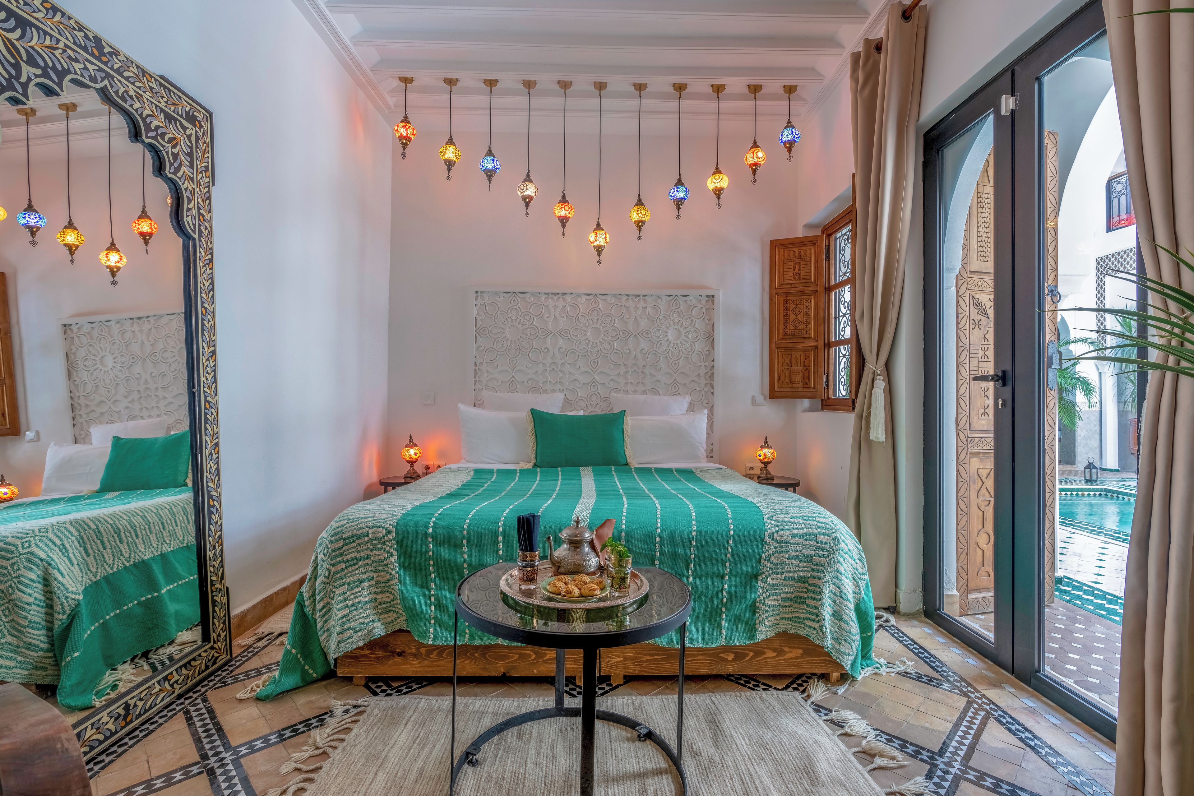 Habitación de hotel con dos camas, una mesa de comedor, luces decorativas colgantes y vista a una piscina.