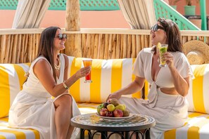 Two people sitting on a striped yellow and white sofa, holding drinks and a plate of fruit. - Riad Nelia Signature (Marrakech)
