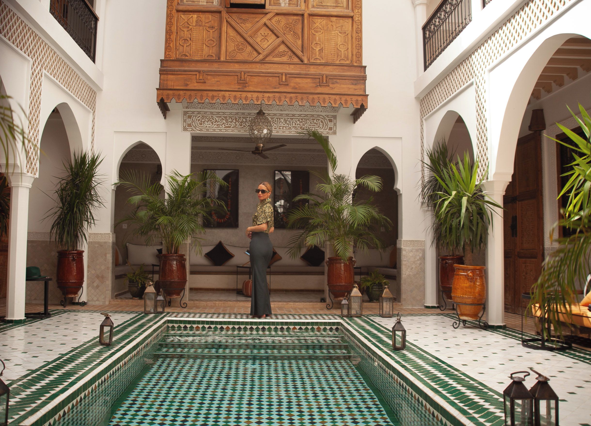 A courtyard with a pool, potted plants, and a person standing in the center.