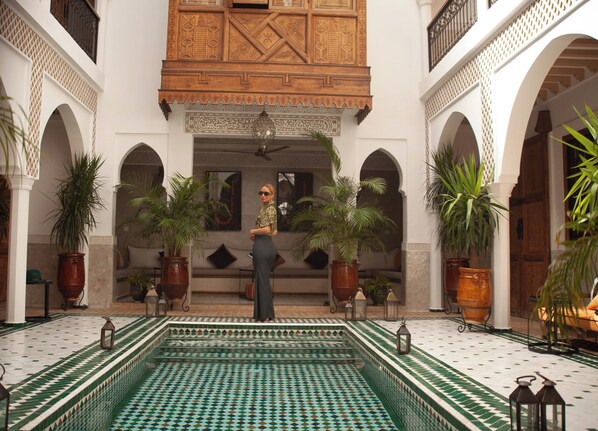 A courtyard with a pool, potted plants, and a person standing in the center. - Riad Nelia Signature (Marrakech)