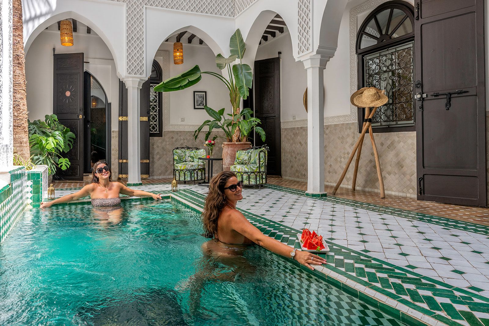 A pool area with tiled flooring, archways, and potted plants.