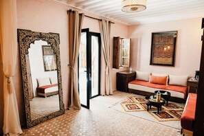 A room with a large ornate mirror, a sofa with orange cushions, a patterned rug, and a small table with a bottle and glasses. - Riad Nelia Signature (Marrakech)