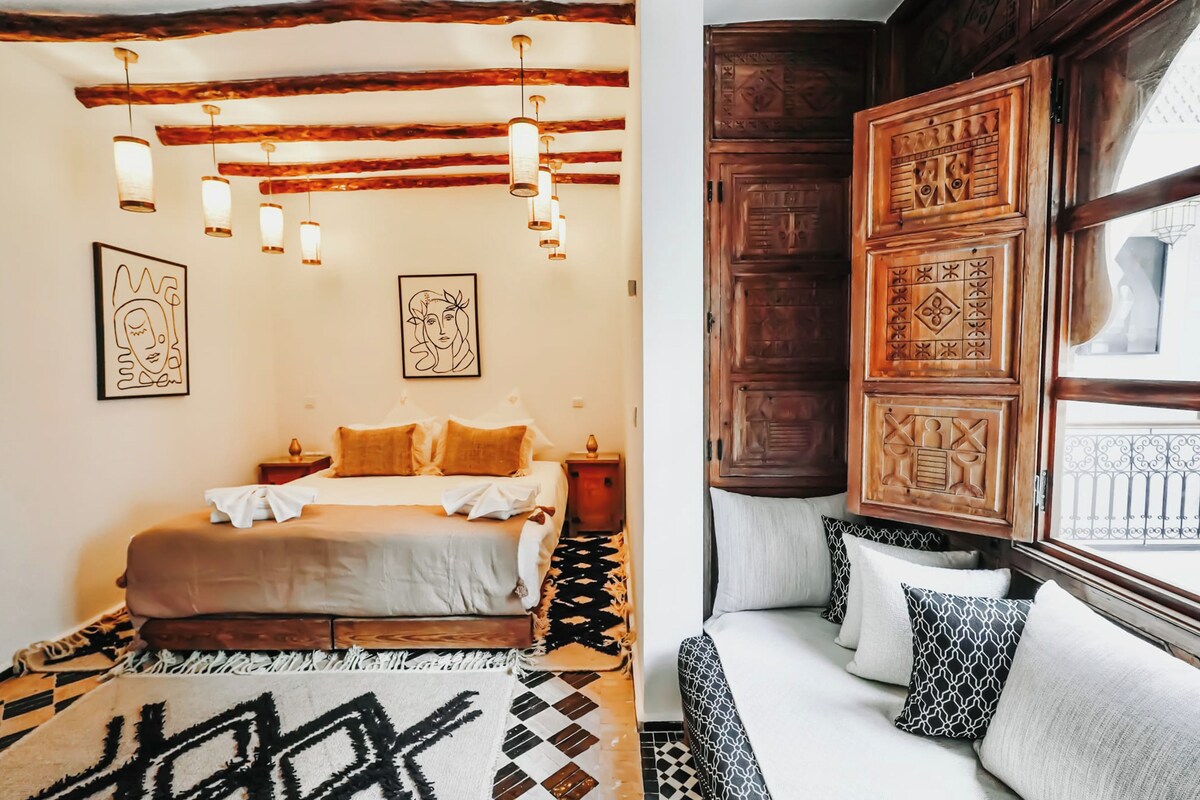 A bedroom with a bed, bedside tables, hanging lights, and patterned rugs.