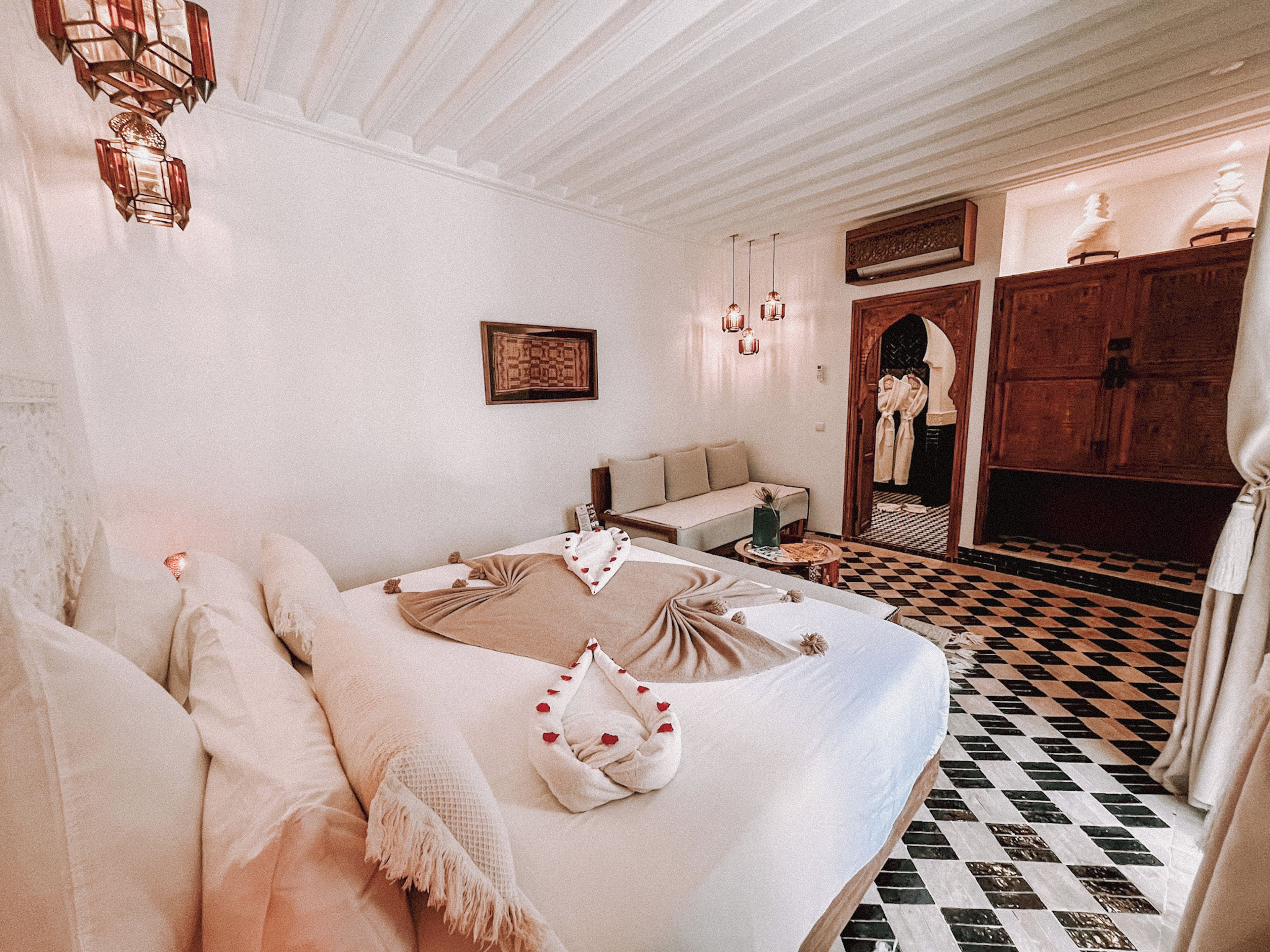 A hotel room with a bed, a sofa, a checkered floor, and a wooden wardrobe.