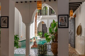 Un área de piscina interior lujosa, con suelo de baldosas, rodeada de arcos y plantas en macetas.