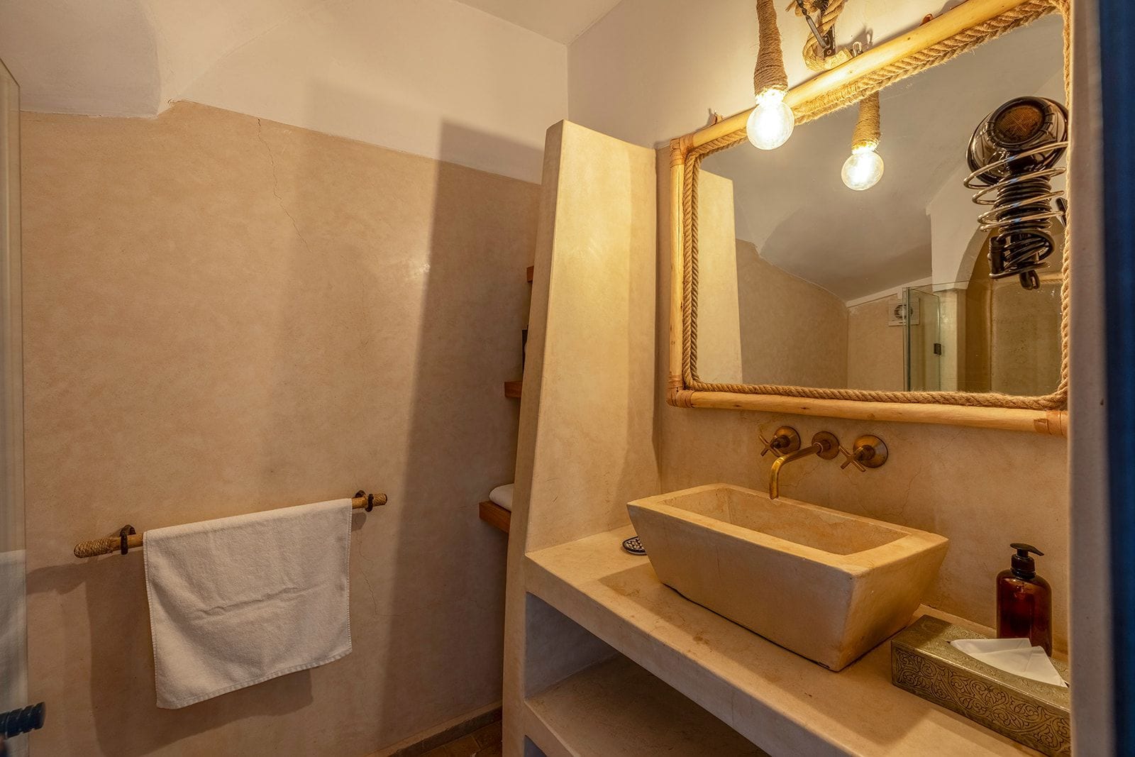 A bathroom with a beige sink, a mirror with a rope frame, and a towel hanging on a towel rack.