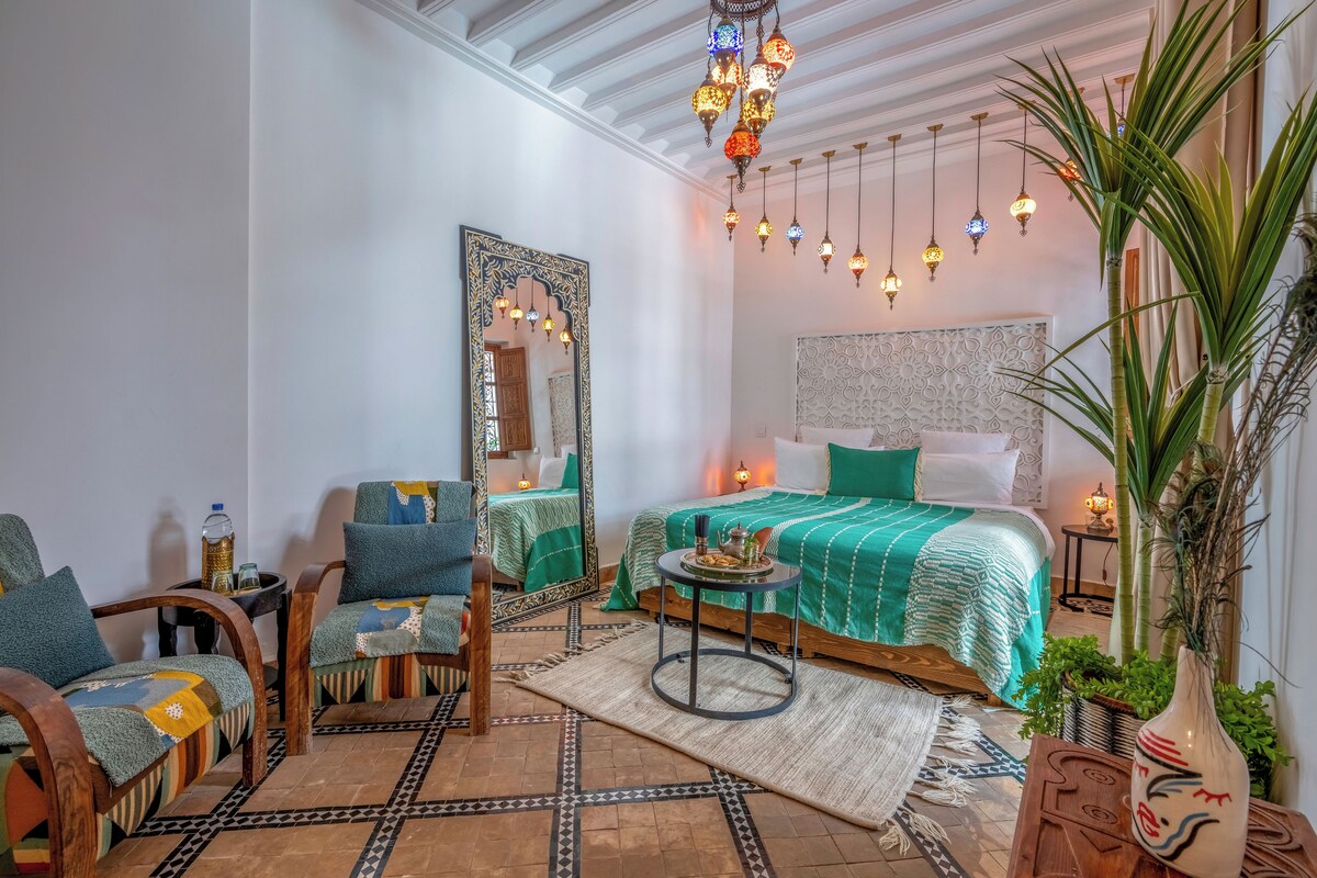Una stanza con un letto, due sedie, uno specchio, un tavolo e lampade a sospensione.