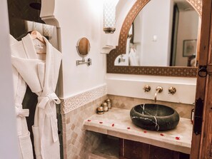 Ein Badezimmer mit Marmorwaschbecken, einem Spiegel mit dekorativem Rahmen und einem auf einem Wäscheständer hängenden Bademantel.