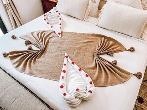 Un lit bien fait, avec une couverture marron et des oreillers blancs décorés de motifs en forme de cœur rouge.