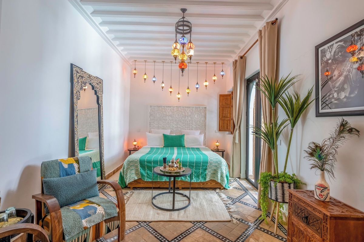 A cozy bedroom with a bed, a chair, a table, and a hanging light fixture.