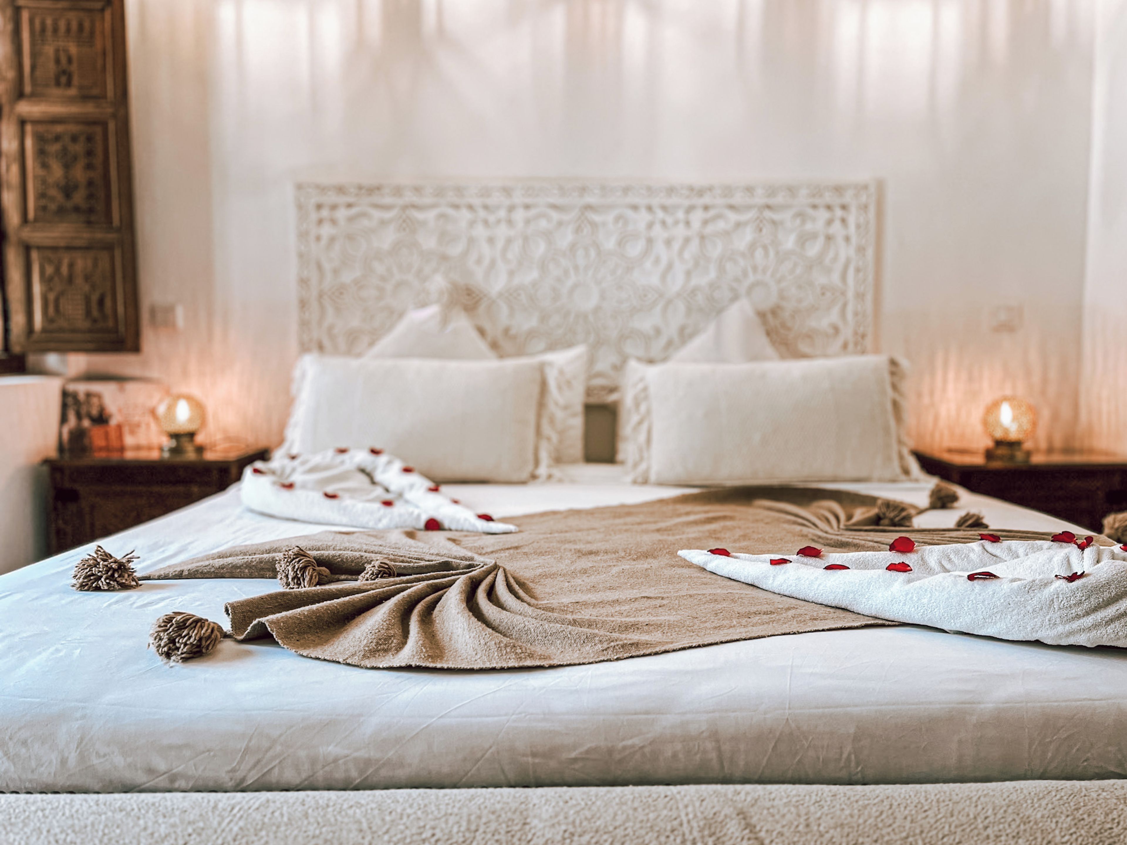 Een net opgemaakt bed met een beige deken, kussens en decoratieve elementen zoals bloemen en een touw.