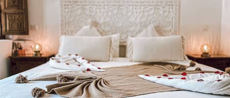 Una cama bien tendida con un edredón color beige, almohadas y detalles decorativos como flores y una cuerda.