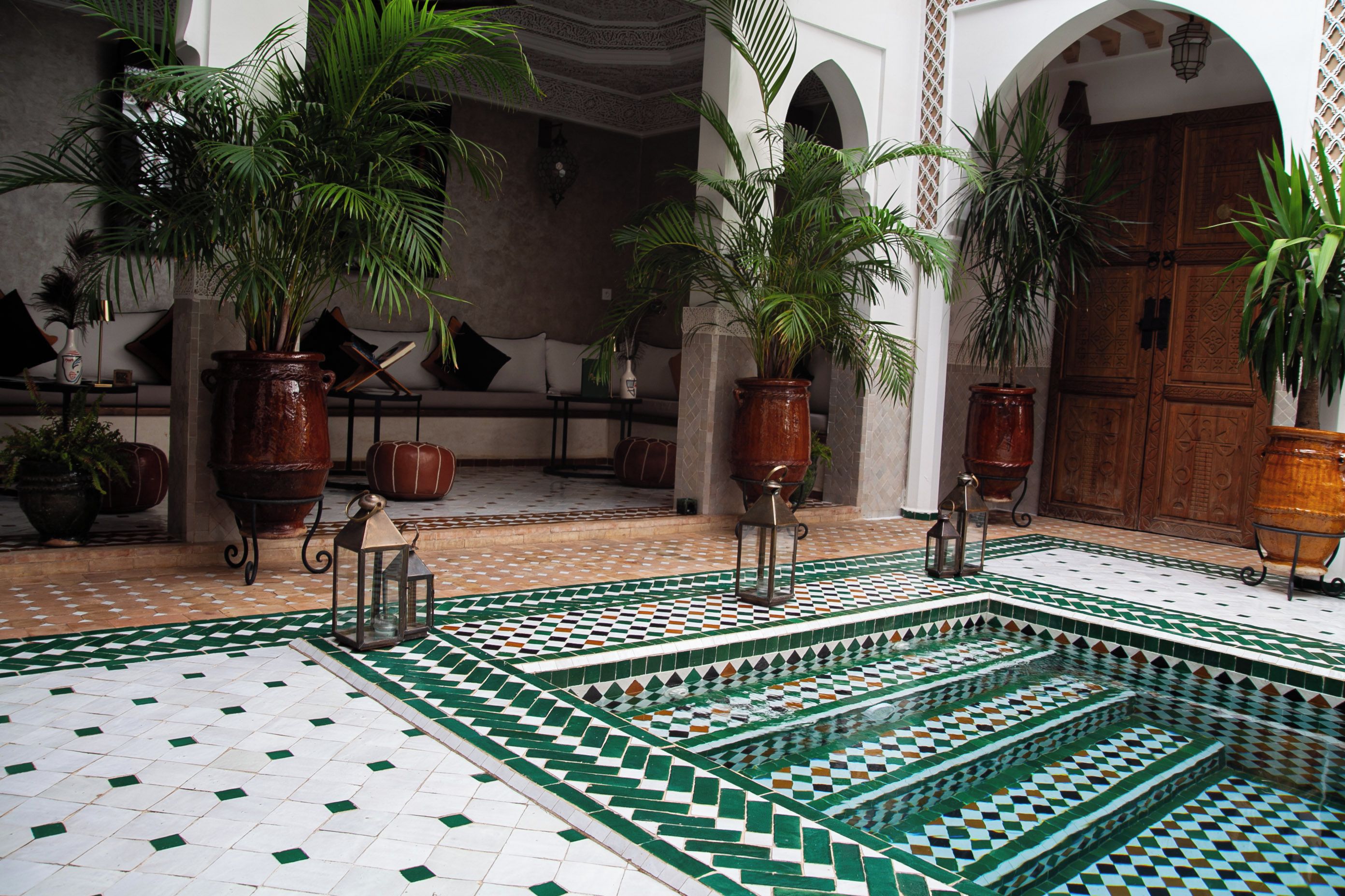 Ein Innenhof mit bepflanzten Kübeln, einem gefliesten Pool und einer Holztür.