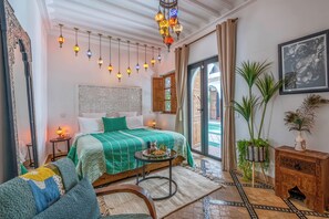 Un dormitorio con una cama a rayas verdes, luces decorativas colgantes, una mesita de noche de madera y vistas al patio.