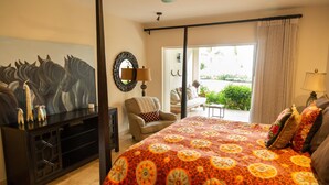 Hotelkamer met een groot bed, een stoel, een televisie, een spiegel en een balkon met uitzicht op groen.