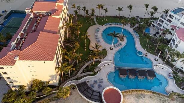 Een resort met een groot zwembad, palmbomen en een strand.