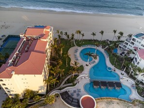 Resort com uma piscina grande, palmeiras e praia.