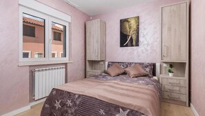 Een slaapkamer met een bed, een raam, een radiator en een aan de muur bevestigd schilderij.