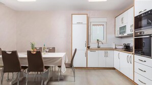 Een moderne keuken met witte kasten, roestvrijstalen apparatuur, en een eethoek met een tafel en stoelen.