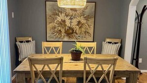 Une salle à manger avec une table en bois, quatre chaises, un luminaire suspendu et un tableau au mur.