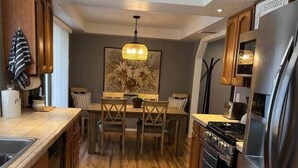 Une cuisine moderne avec des meubles en bois, un réfrigérateur en acier inoxydable, une table à manger avec des chaises et un lustre.