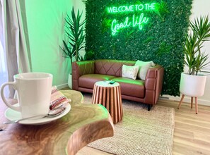 A cozy living room with a brown sofa, a wooden coffee table, and a neon sign that reads "WELCOME TO THE Good life". - Barossa Palms Motel (Nuriootpa)