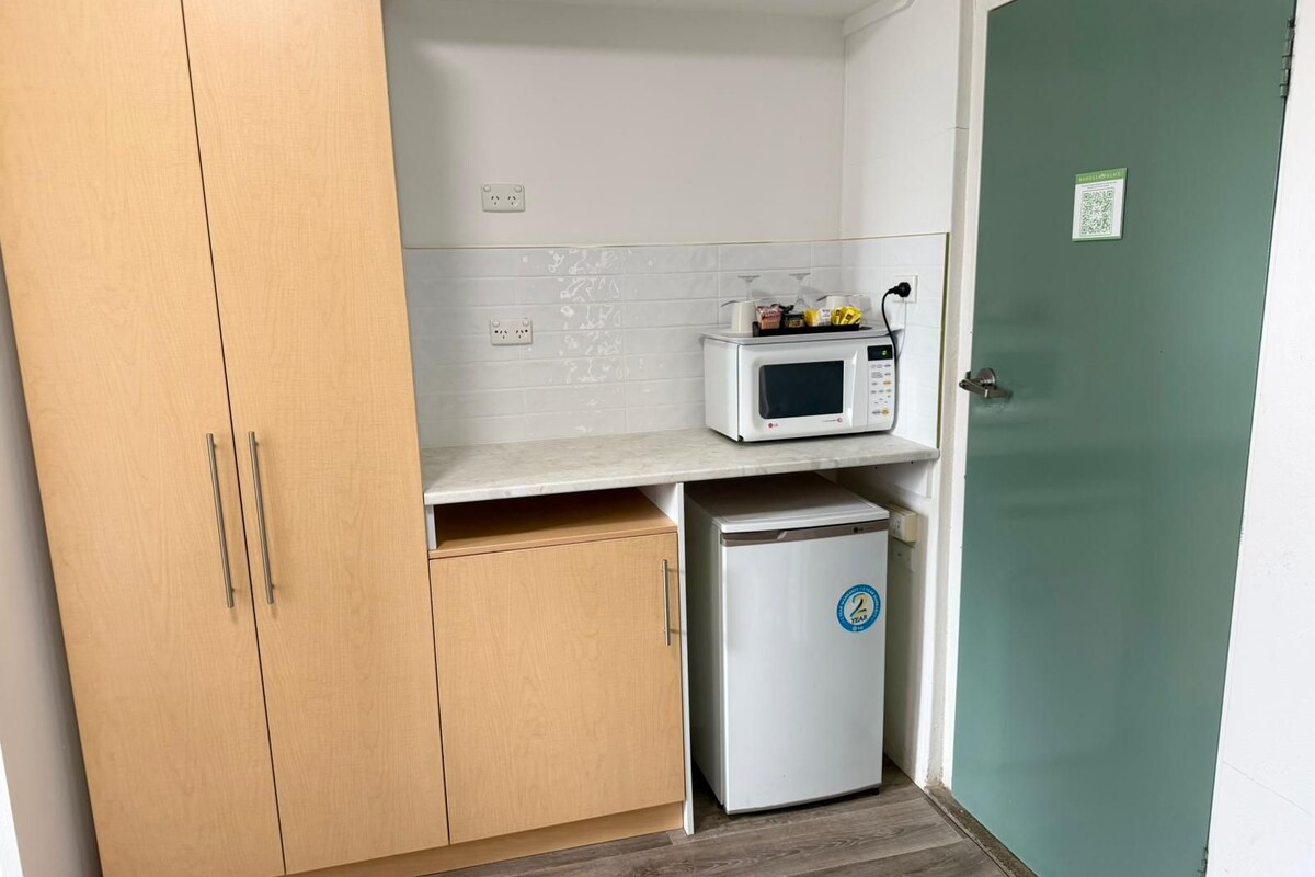 A compact kitchenette with a microwave, a small refrigerator, and wooden cabinets.