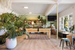 A pool table in a room with wooden flooring, surrounded by potted plants and shelves with books and decorative items. - Barossa Palms Motel (Nuriootpa)