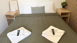 Una camera d'albergo con un letto, cuscini, un tavolino, una lampada da parete e una pianta in vaso.