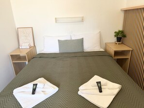 Ein Hotelzimmer mit Bett, Kissen, einem Nachttisch und einer Wandleuchte, dazu eine Zimmerpflanze.