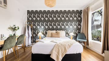 A modern bedroom with a large bed, a desk, two chairs, a window with curtains, and a patterned wall.
