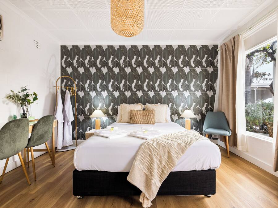 Une chambre moderne avec un grand lit, un bureau, deux chaises, une fenêtre avec des rideaux et un mur décoré de motifs.